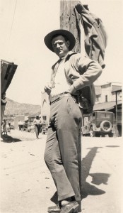 A man in a cowboy hat, displaying vital characteristics, leans against a pole.