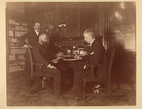 Three men sitting at a desk, ready to give and take criticism.