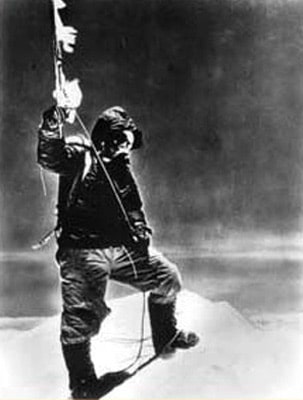 An adventurous man triumphantly stands atop a majestic mountain, proudly holding a flag.