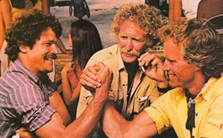 A group of men are sitting around a table engaging in intense arm wrestling, determined to dominate their opponents for the top spot.