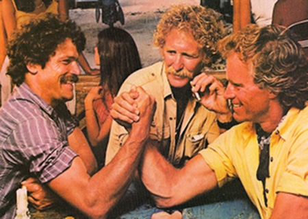 A group of men are sitting around a table engaging in intense arm wrestling, determined to dominate their opponents for the top spot.