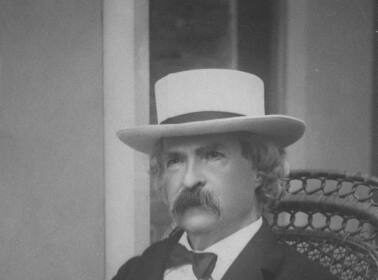 A man in a hat and bow tie sitting in a chair.