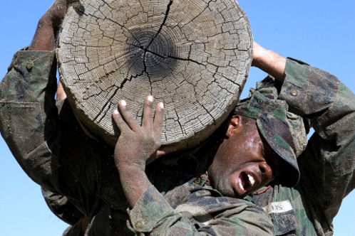 A Navy Seal is carrying a large piece of wood, embodying the creed.