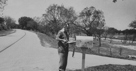 An old black and white photo of a man standing next to a mailbox, capturing the art of letter writing and possibly reflecting the sentiment of a sympathy note.