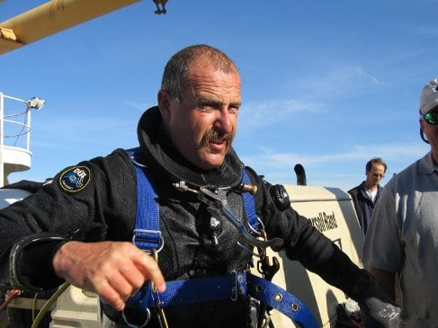 A Deep Sea Diver in a diving suit standing next to a boat.