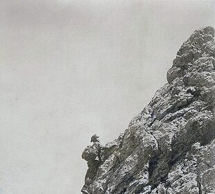 Two men engaged in mountaineering, climbing up the side of a mountain.