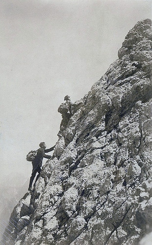 Two men engaged in mountaineering, climbing up the side of a mountain.