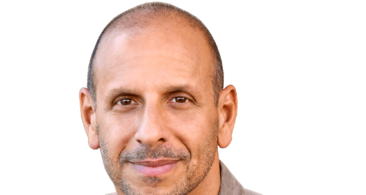A man in a gray shirt is smiling during an interview for BetterMen.org.