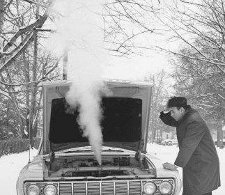 A man examining the hood of a car in the snow.