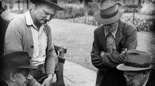 A group of men indulging in a manly hobby, playing chess in a park.