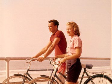 A man and woman, dressed in summer attire, standing on a boardwalk with bicycles.