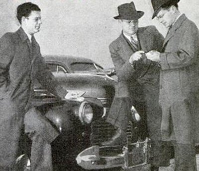 Three men negotiate next to a used car.