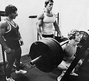 Three Gym Junkies standing next to a barbell in a gym.