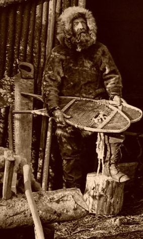 A man with a sled in front of a log cabin, embracing the Legends of the Northwest.