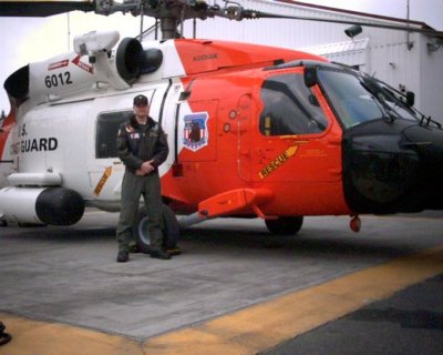 A Coast Guard Helicopter Flight Mechanic standing next to an orange and black helicopter.