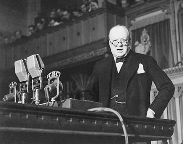 A man in a suit demonstrating classical rhetoric while standing in front of a microphone.