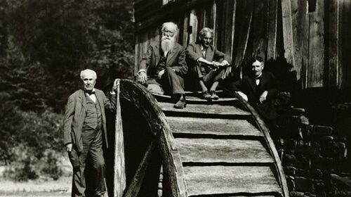 Three men demonstrating the power of cooperation as they stand on top of a water wheel together.