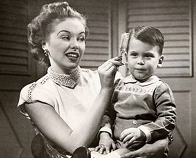 An old black and white photo capturing the tender moment of a woman brushing a child's hair.