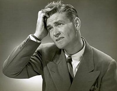A black and white photo of a man with his hand on his head, showcasing an expression of exasperation.
