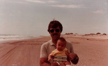 A man embracing life while tenderly holding a baby on a vibrant beach.