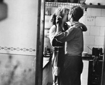 An old black and white photo of a man and woman at-home dinner date in a kitchen.