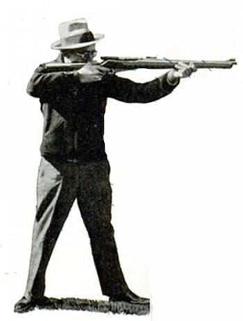 A man with a hat is holding a rifle, ready to shoot.