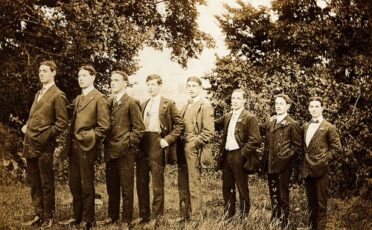 A group of tall men in suits standing in a field.