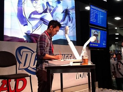 A Comic Book Artist at a table signing a comic book.