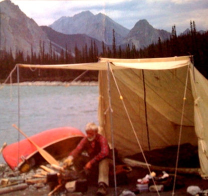 An unconventional man in a tent next to a canoe on a lake.