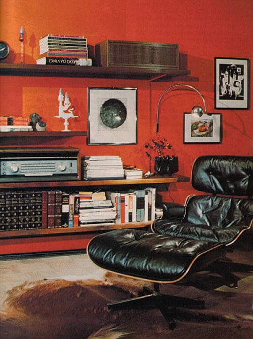 A black lounge chair in a man room with red walls, decorated to perfection.