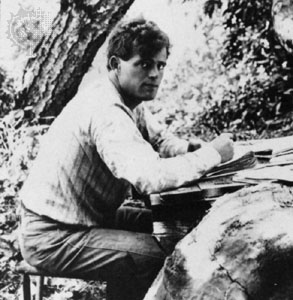 A man writing at a table in the woods.