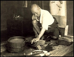 An old black and white photo of a man working with tools on a wooden table.