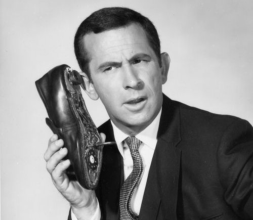 An old black and white photo of a man holding a shoe, showcasing his cool spy concealments.