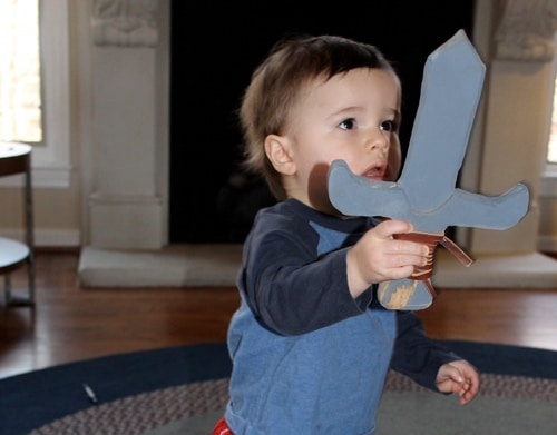 A kid wielding a wooden sword in front of a fireplace during a weekend DIY project.