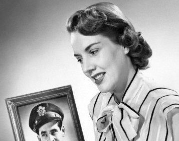 A woman gazes affectionately at a picture of a man in uniform, immersed in the romance it represents.