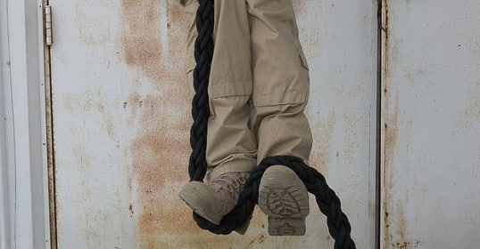 A man is hanging on a rope from a door as if he were a Navy SEAL training to climb.