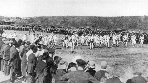 A crowd of people watching a long distance race on a dirt field, offering a beginner's guide.