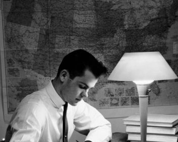 A successful man utilising study tactics, writing at a desk with a lamp during exams.