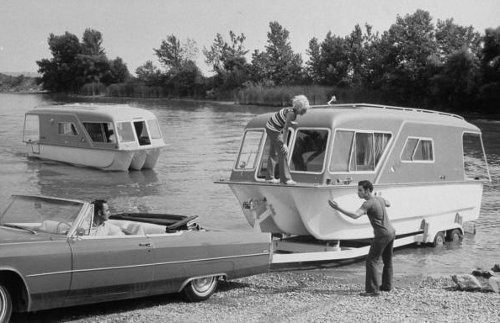 An old photo of a man towing a camper trailer.