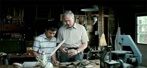 Walt Kowalski, an old man, works with a toolbox in his workshop alongside a young man.