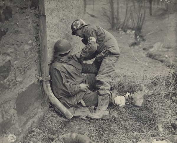 An old photo of a Combat Medic helping another soldier.