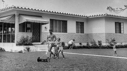 A black and white photo of children playing in the yard of a house.