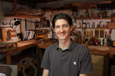 A skilled luthier sitting in a workshop surrounded by a variety of tools, crafting exquisite guitars.