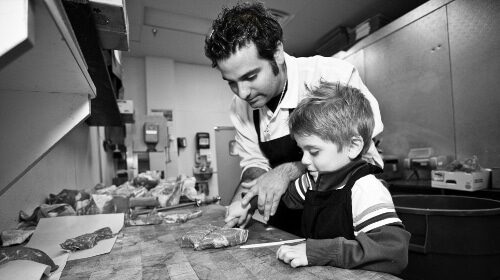 A butcher and a boy preparing food in a kitchen.