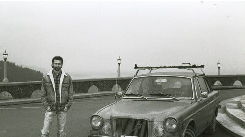 A happy man standing next to his car on a bridge.