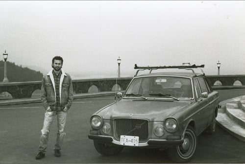 A happy man standing next to his car on a bridge.