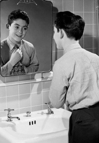A young child looking at himself in the mirror.