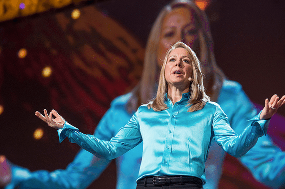 In a blue shirt, a woman stands in front of a large screen.