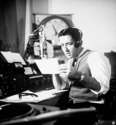 A man in a radio studio reading a letter for his podcast on the Art of Manliness.
