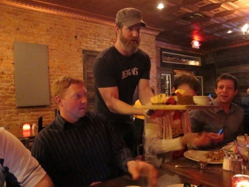 The restaurant owner is holding a tray of food in front of a group of people.